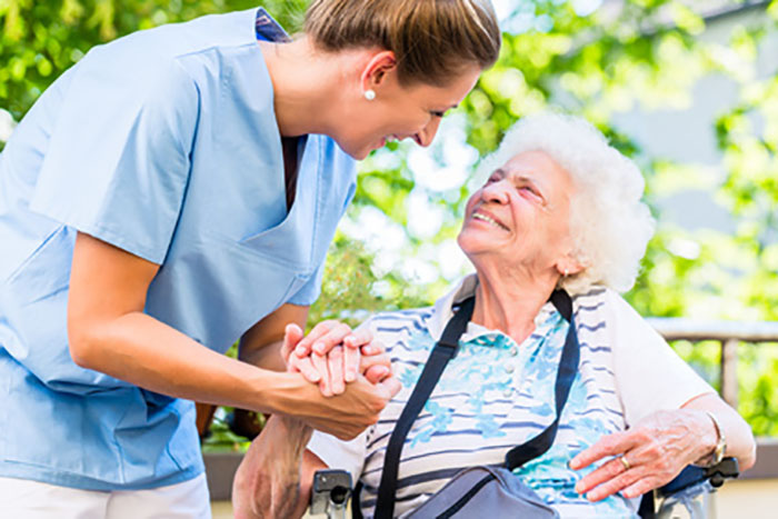Pflegerin hält die Hand einer Seniorin und lächelt