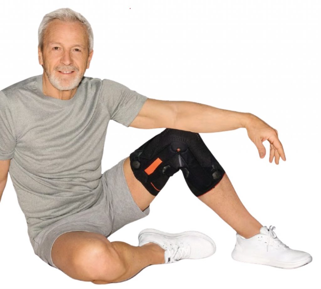 Älterer sportlich aussehender Mann sitzt in lockerer Haltung auf dem Boden und trägt eine Kniebandage